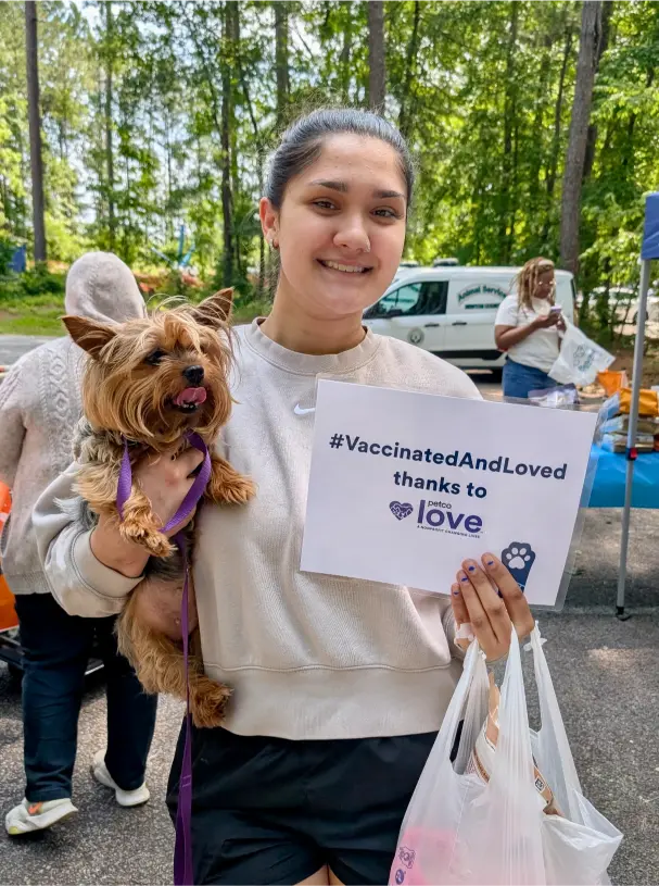 A Newton county resident holding her dog and a sign that says, "#VaccinatedAndLoved thanks to Petco Love."